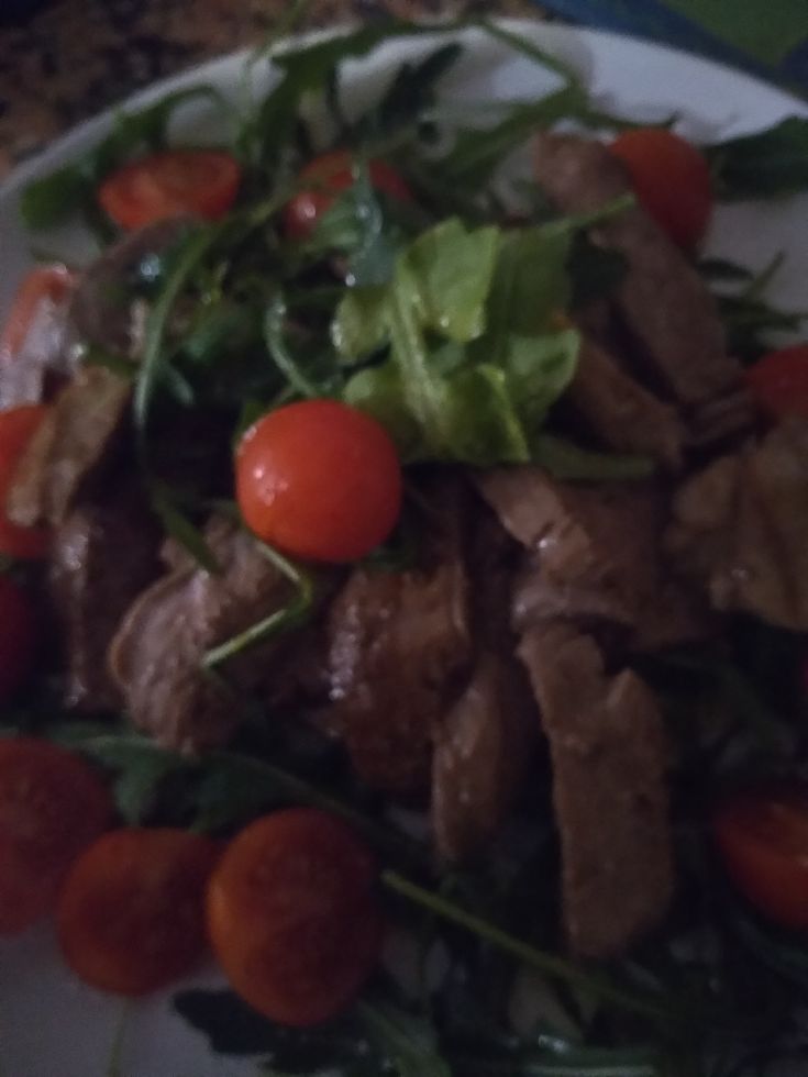 A meat dish served on a bed of arugula with fresh cherry tomatoes, perfect for a light and nourishing meal.
