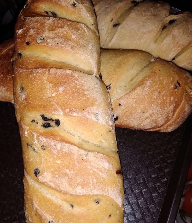 Freshly baked artisanal bread loaves, golden and enriched with olives, perfect for meal accompaniment.