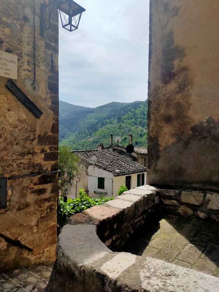 Scene of an ancient village with stone buildings and green mountains in the background.