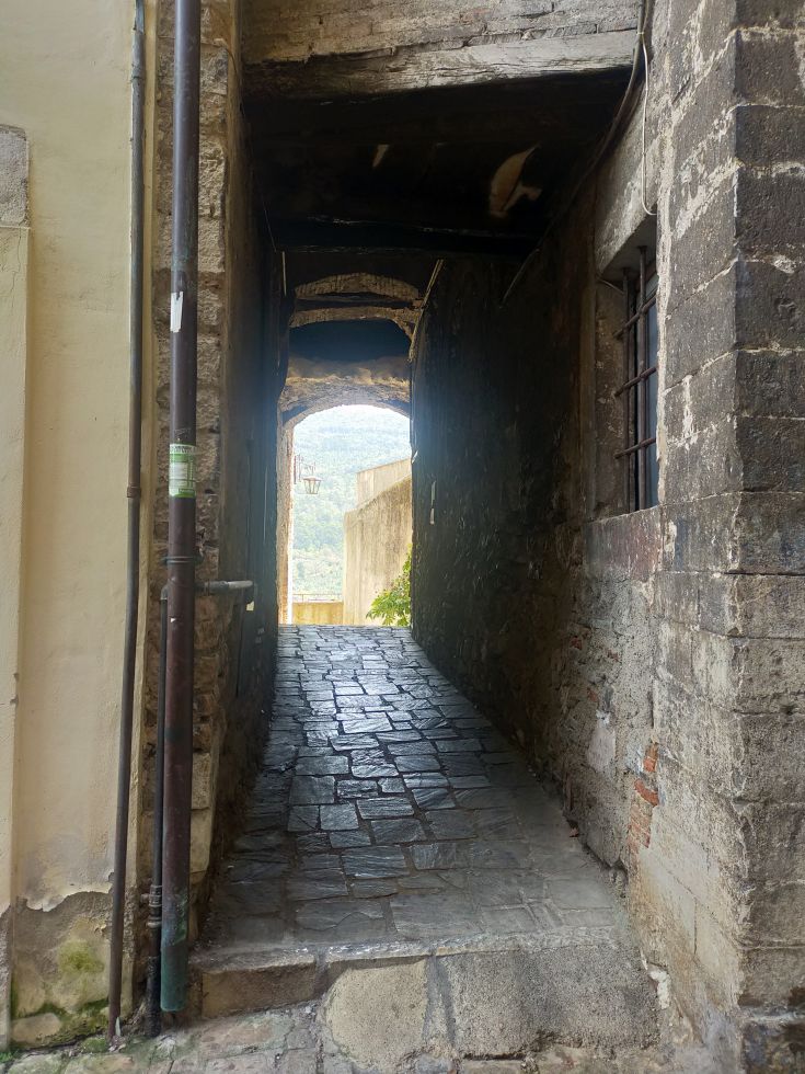 A narrow alley leading to a light source, with stone walls bordering both sides.