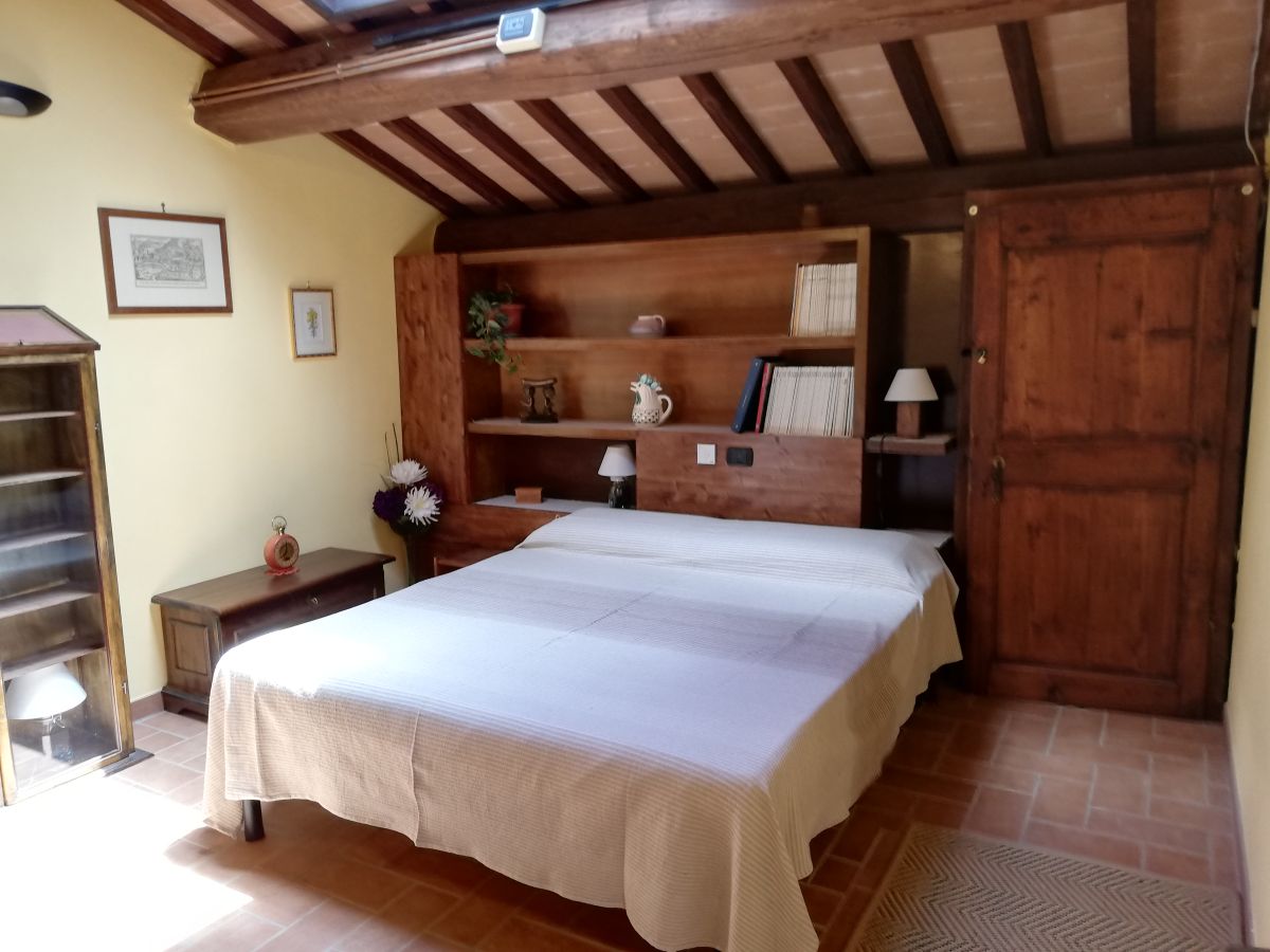 Mansarda accogliente con letto matrimoniale e mobili in legno, circondata dalla natura umbra.