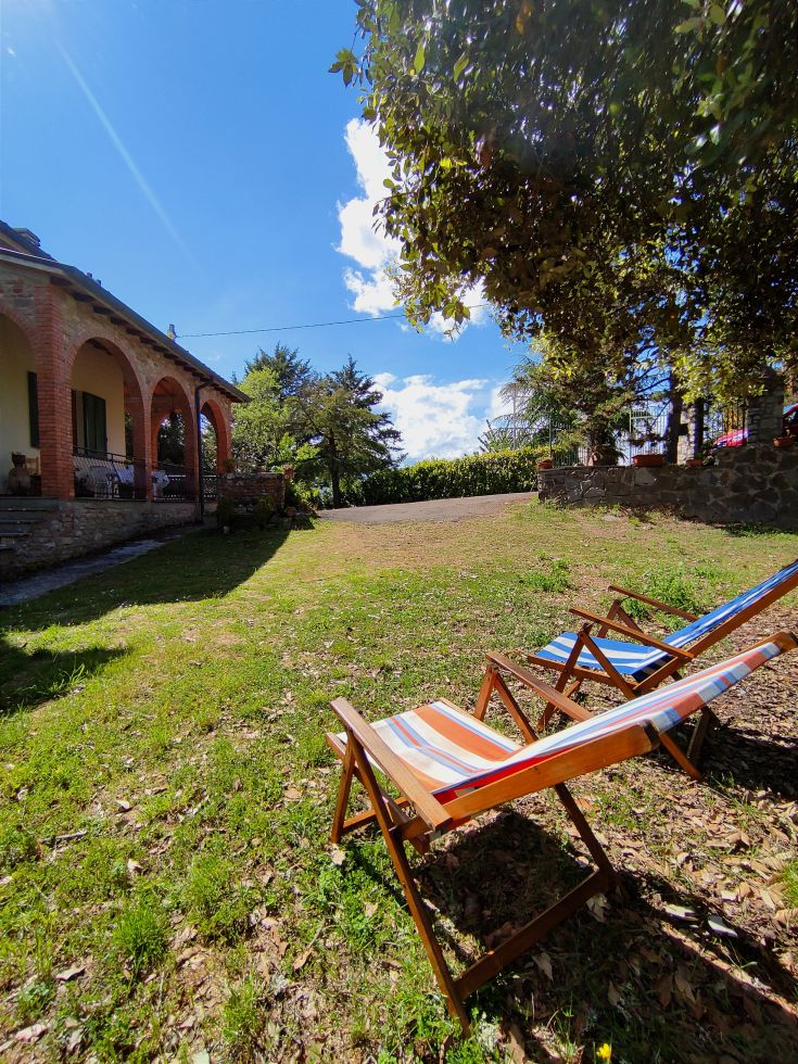 A well-maintained villa surrounded by greenery, with comfortable sun loungers available in the garden.