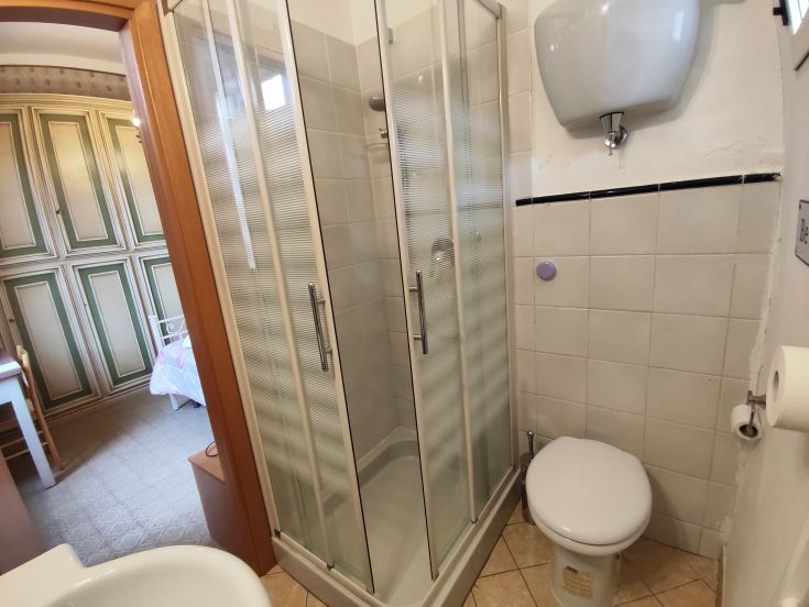 A simple bathroom with a shower, toilet, and sink, decorated with light-colored tiles.
