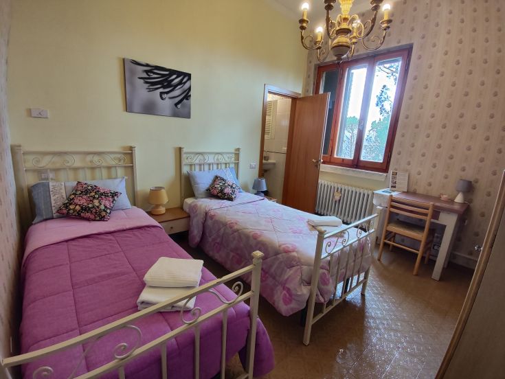 Bright room with twin beds, simple and functional, featuring a wardrobe and a window.