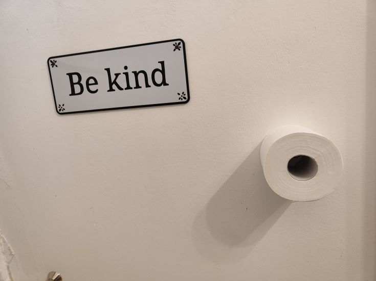 A sign encouraging kindness, placed next to a roll of paper. Simple environment.