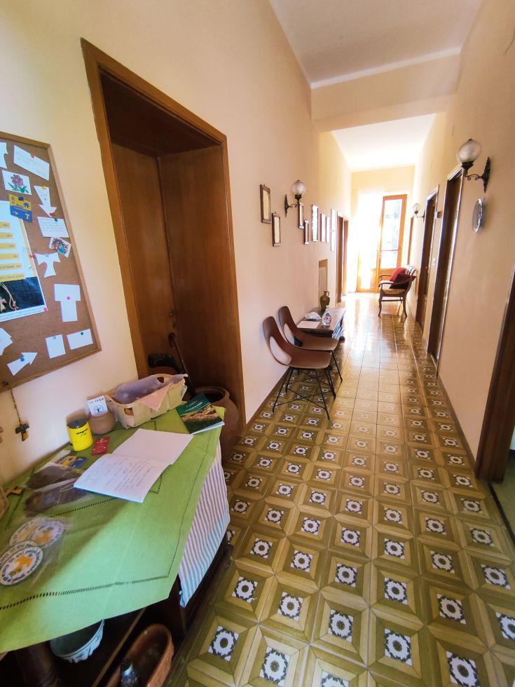 A spacious corridor with various doors, paintings on the walls, and a table adorned with small decorative items.