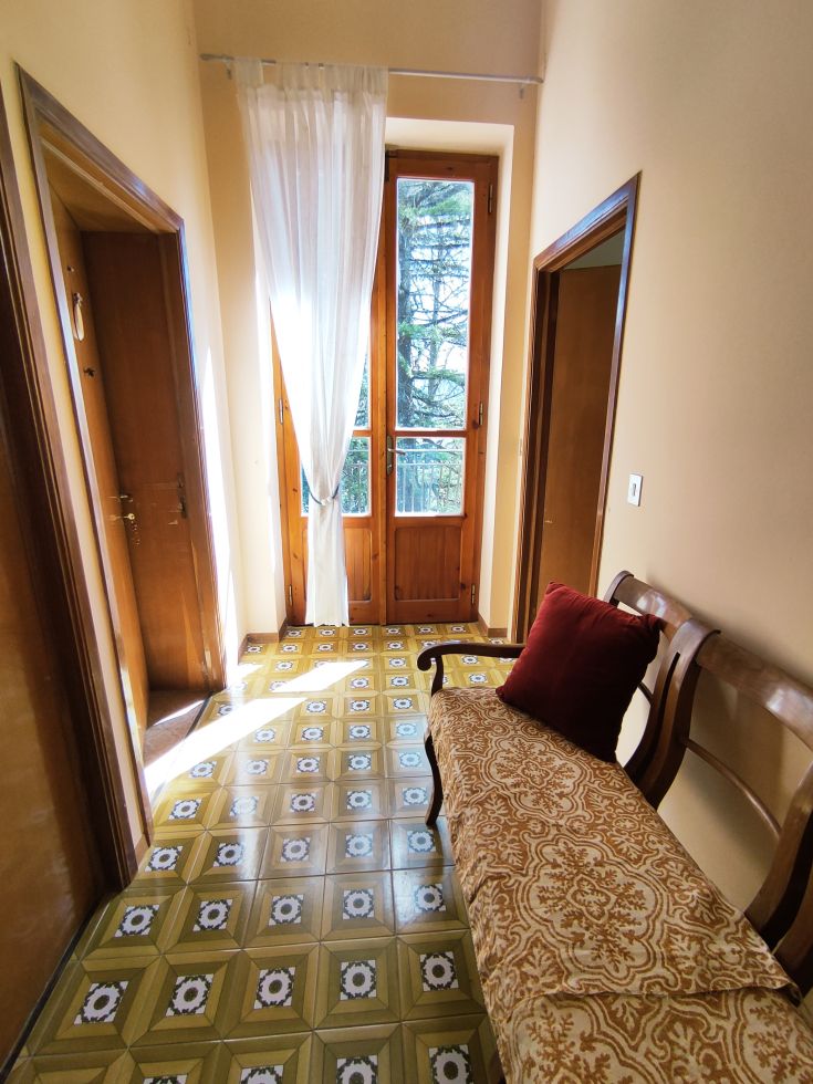A quiet corridor with tiled flooring and windows allowing natural light to enter.