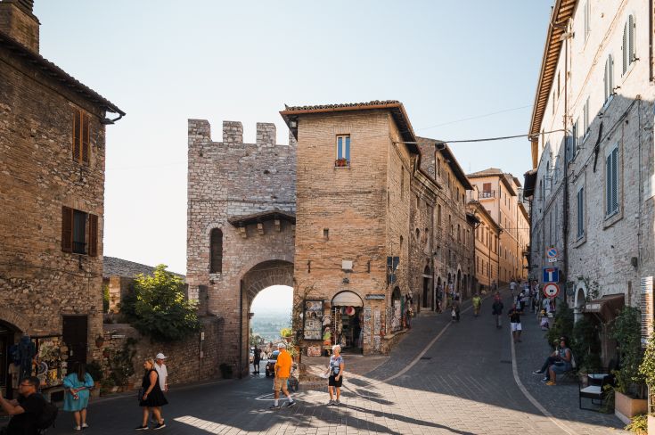 Eine charakteristische Ecke von Assisi, mit historischen Gebäuden und sich bewegenden Menschen, die eine familiäre Atmosphäre schaffen.
