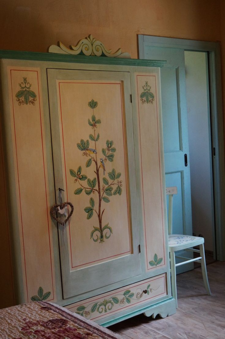 Armadio in stile rustico con decorazione floreale, collocato in un ambiente semplice e accogliente.