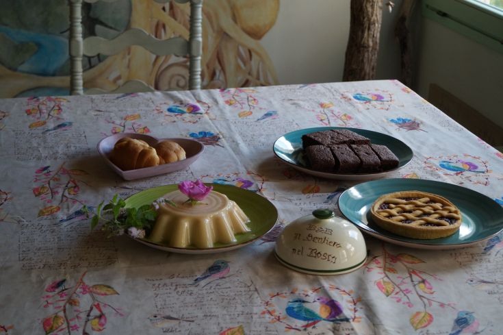 Un tavolo ben apparecchiato con dolci assortiti e una semplice decorazione floreale, ideale per una pausa in un ambiente rurale.