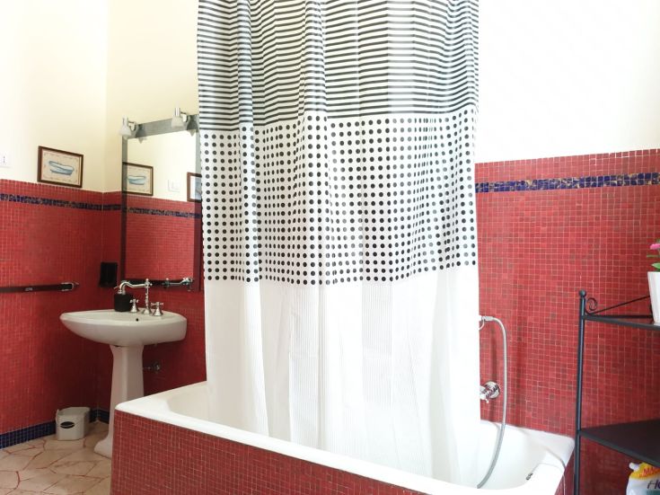 Un bagno con pareti rosse, dotato di doccia con tendaggio decorato a righe e pois.