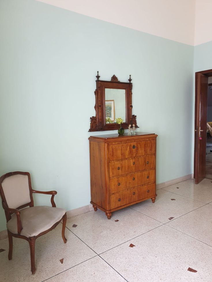 Interno di un edificio con arredi in legno, uno specchio e pareti azzurro chiaro.