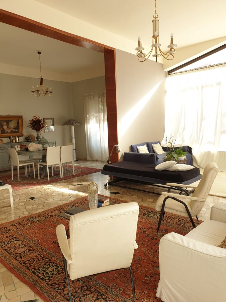 Un soggiorno spazioso e luminoso, caratterizzato da arredi semplici e una grande vetrata. L'ambiente è accogliente e armonioso.