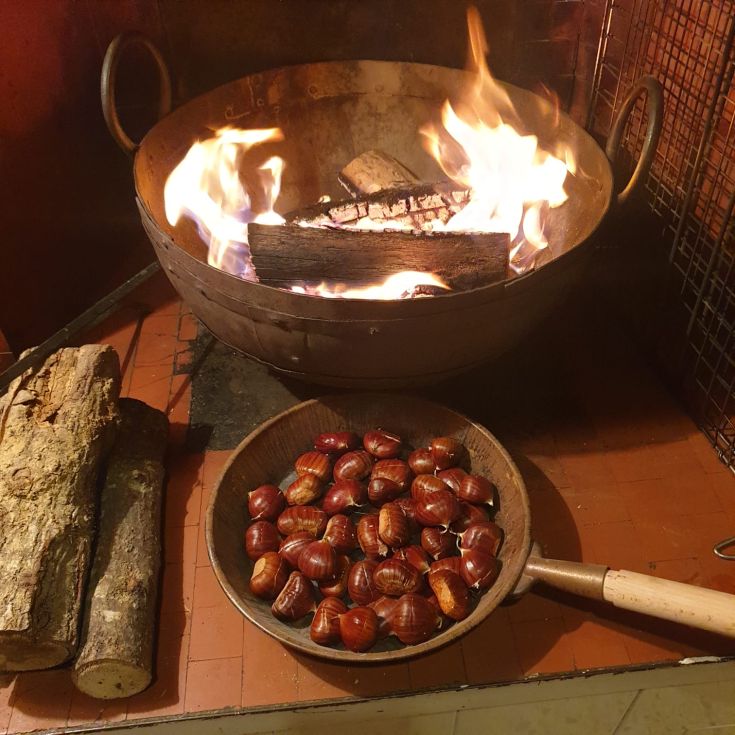 Un camino caldo con castagne arrostite e legna pronta per il fuoco.