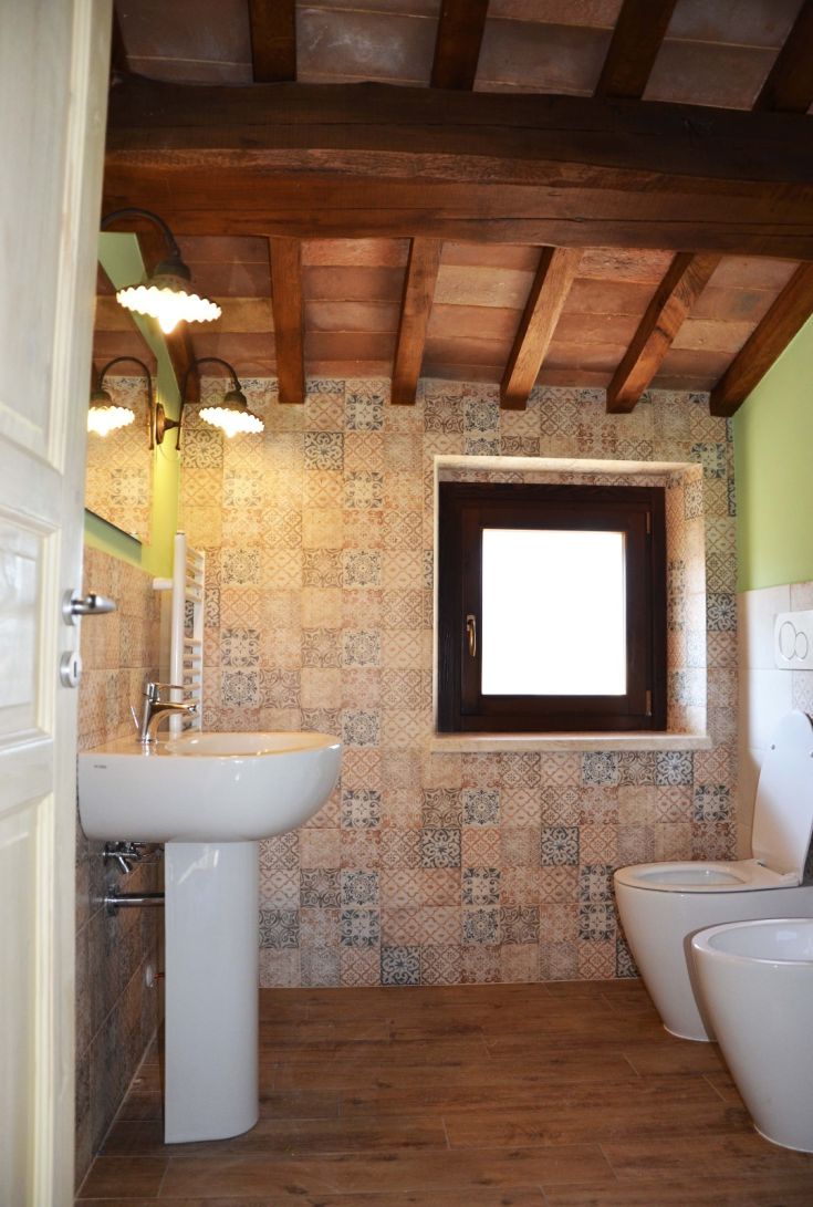 Bagno semplice con finiture in legno e piastrelle decorate, ben illuminato e dal design accogliente.