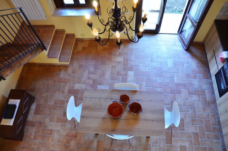 Ambiente tranquillo con un tavolo di legno e stoviglie, illuminato da un lampadario semplice.