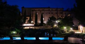A tranquil night atmosphere with an illuminated pool, surrounded by greenery in a renovated historical building.