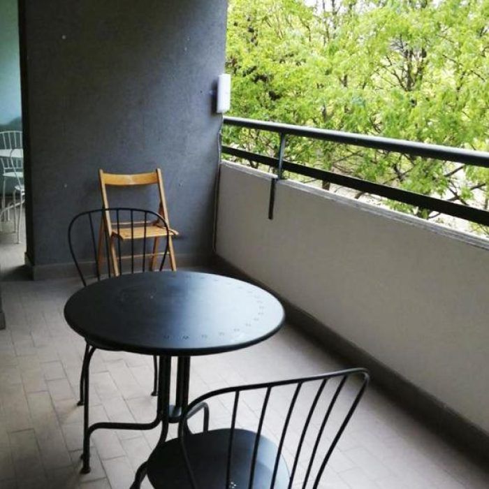 A green balcony with a wooden table and chairs, surrounded by lush green plants.