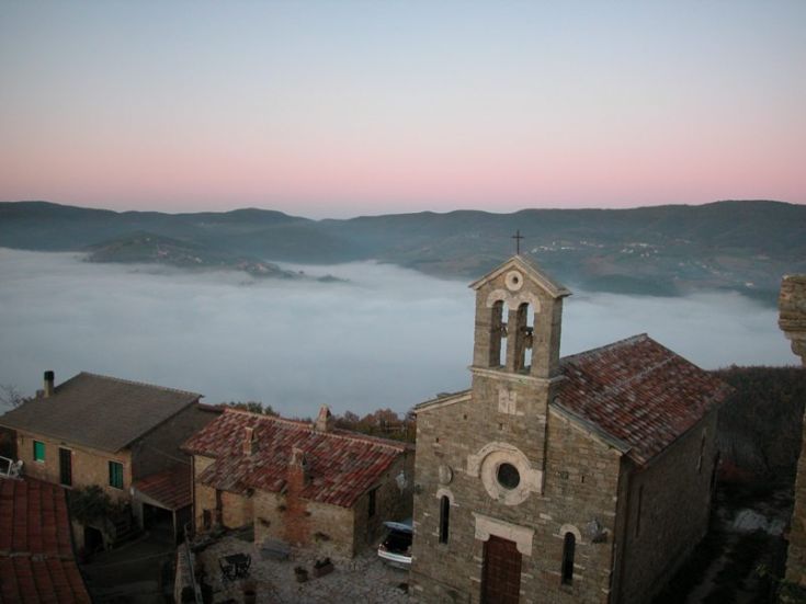 Eine neblige Morgenszene, die ein Dorf zeigt, das in Nebel gehüllt ist, mit einer Kirche im Vordergrund gut sichtbar.