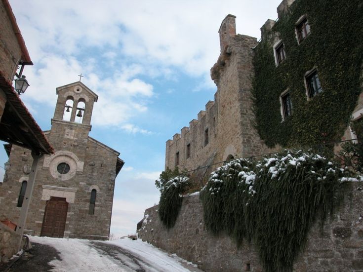 Ein altes Dorf mit einer Kirche und einem Gebäude, umgeben von Bäumen und mit Schnee bedeckt.