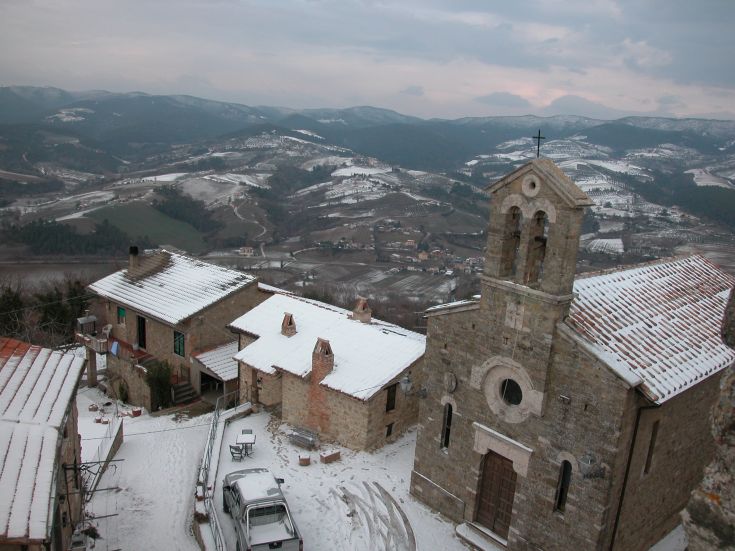 Winterpanorama eines Dorfes mit Steinbauten und einer Kirche, umgeben von Schnee.