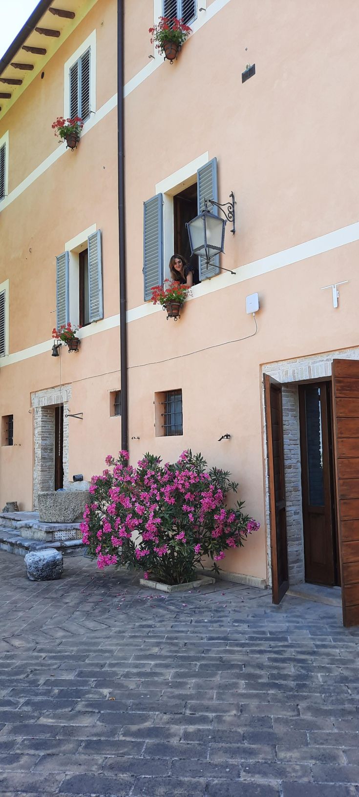 Eine von Blumen geschmückte Landhausfassade mit einer Frau, die sich vom Balkon lehnt.