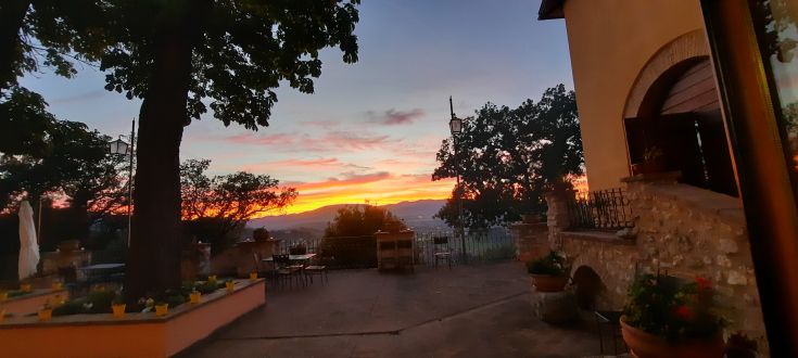 Sonnenuntergangsszene über die Natur von einer großen Terrasse eines Bauernhauses, umgeben von Bäumen und Hügeln.