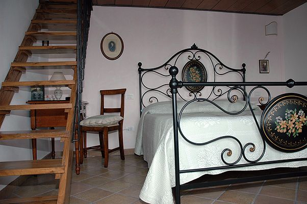 Camera accogliente con letto in ferro battuto e scala in legno, con un'atmosfera calda e confortevole.
