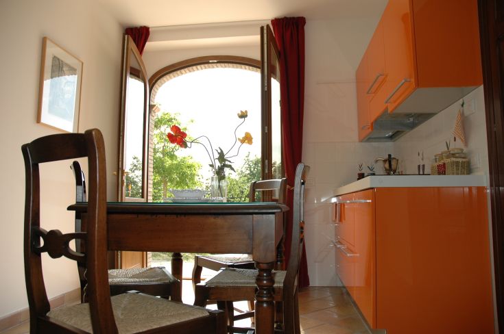 Cucina luminosa con mobili arancioni e panorama su un giardino verde, in un'atmosfera confortevole.