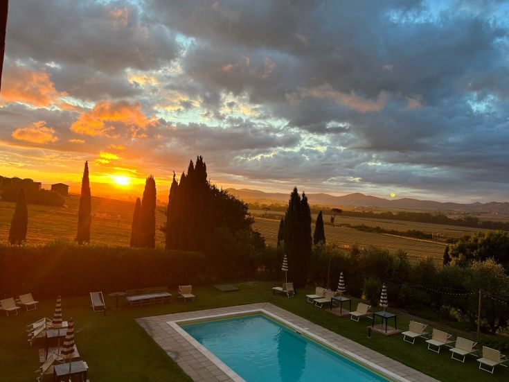 Tramonto sereno su un agriturismo immerso tra cipressi e colline verdi.