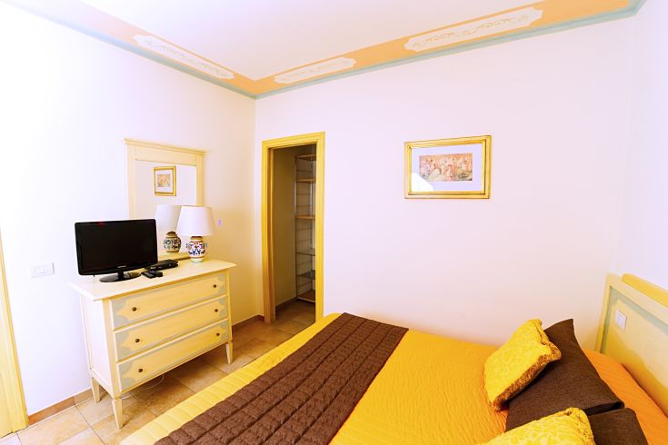 Cozy room with a TV, colorful beds, and simple decorations. Brightly lit and carefully furnished.