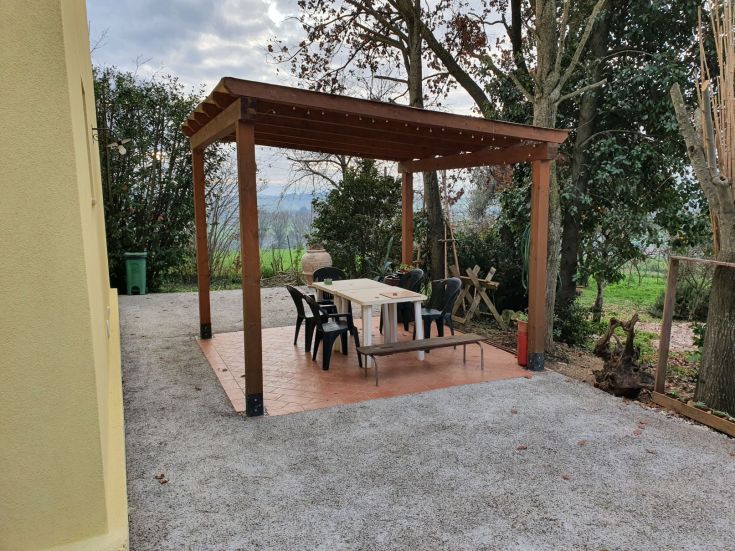 Außenbereich mit einem Holzgazebo und Tisch, umgeben von üppigem Grün.