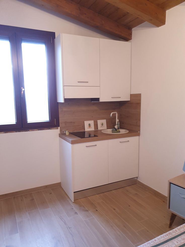 Einfache Küche in einer kleinen Wohnung, ausgestattet mit weißen Schränken und einer Holzarbeitsplatte.