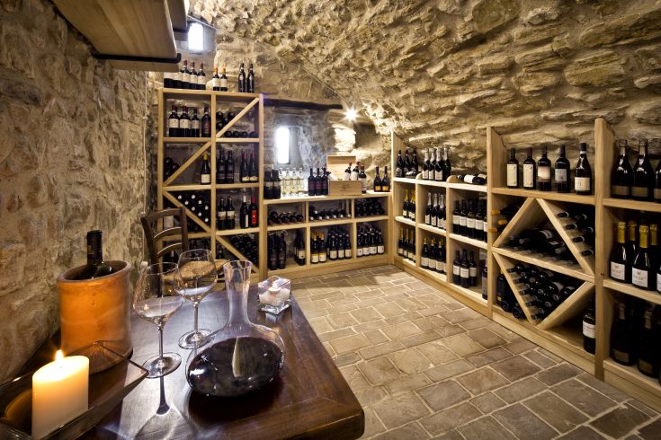 Una cantina con muri in pietra, scaffali in legno ben ordinati e una selezione di vini.