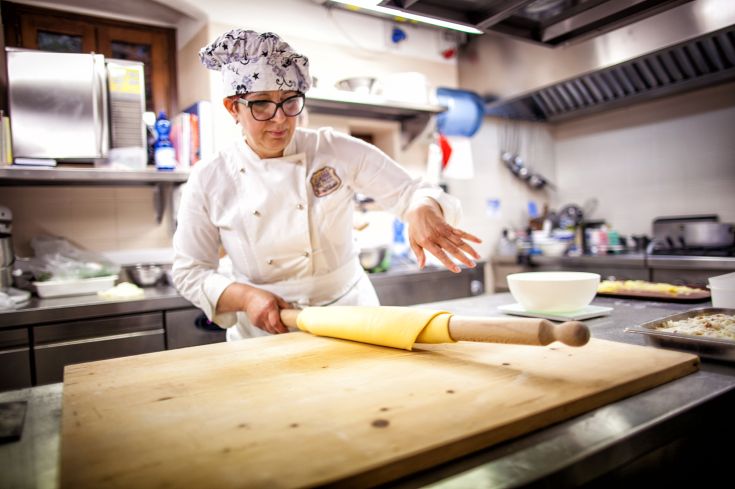 Una cuoca stende la pasta in un ristorante moderno, caratterizzato da un ambiente professionale e accogliente.