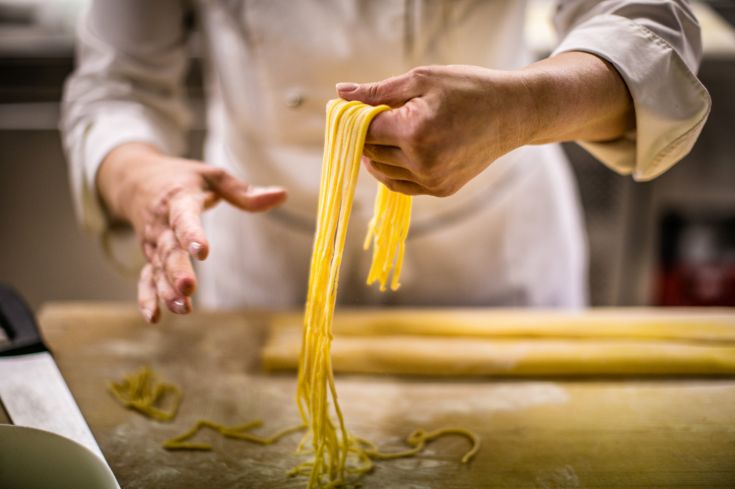 Un cuoco alle prese con la preparazione della pasta fresca, esprimendo abilità e passione culinaria.