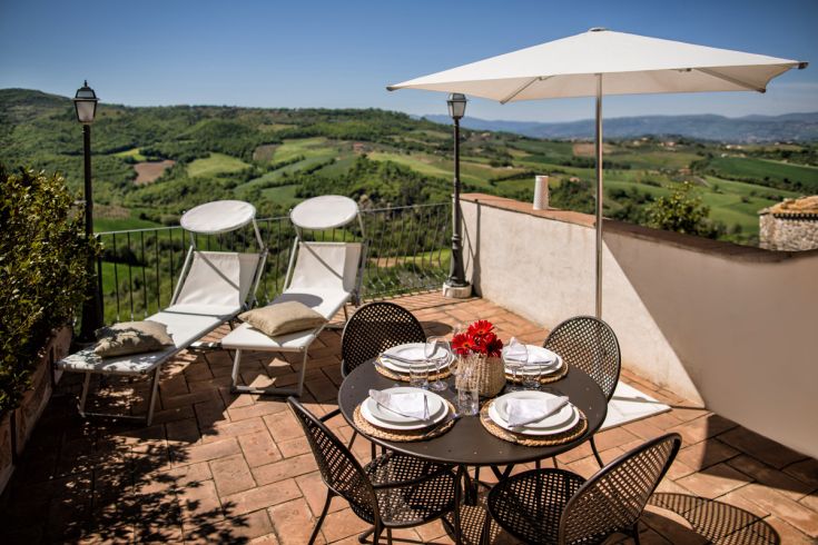 Una terrazza soleggiata con panorama, lettini e un tavolo apparecchiato in modo semplice.