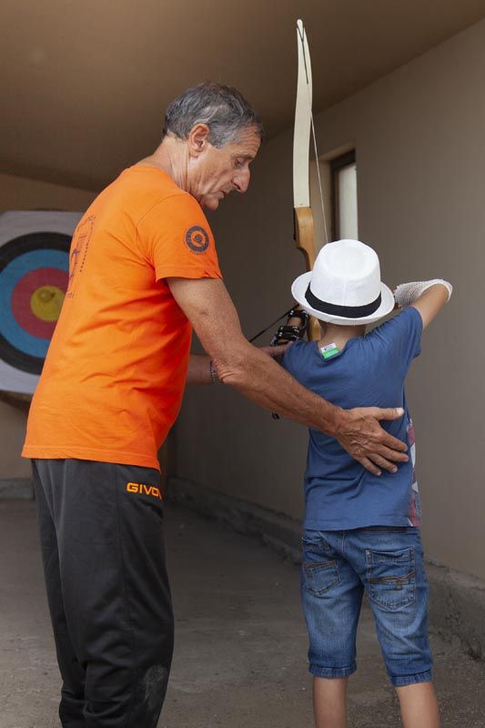 un signore insegna ad un bambino come si tira con l'arco 