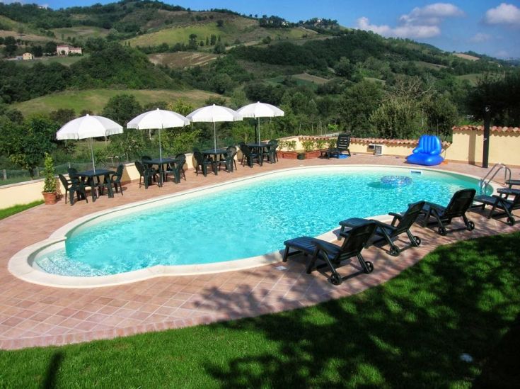 Une piscine avec des chaises longues et des parasols, située dans un paysage vallonné.