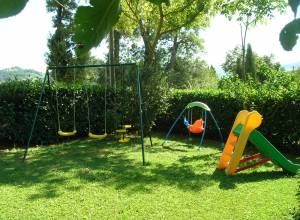 Aire de jeux en plein air entourée d'arbres, avec des balançoires et un toboggan de différentes couleurs.