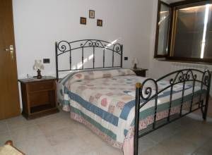 Chambre intime avec un lit double, décorée de manière simple. La lumière naturelle illumine la pièce par la fenêtre.