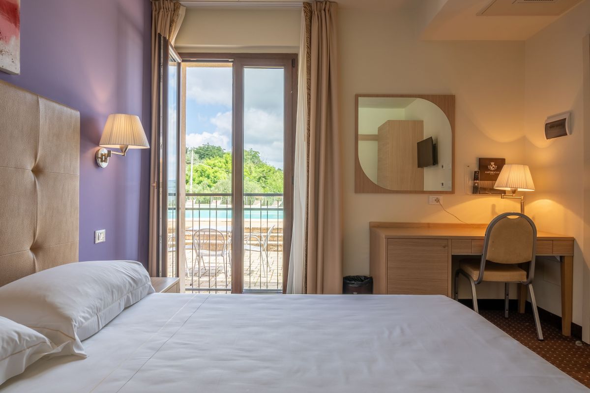 Comfortable hotel room with a view of the pool, featuring simple and functional furnishings.