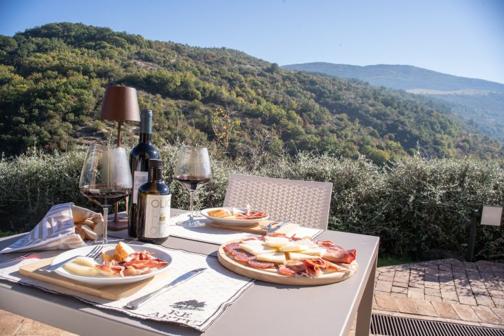 Un tavolo all'aperto con vino e taglieri di salumi e formaggi, circondato dalla natura umbra.