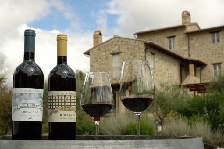 Due bottiglie di vino rosso e due bicchieri su un tavolo in un ambiente rustico vicino a un edificio in pietra.