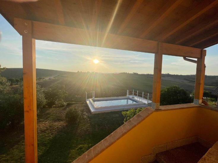 Scena di un agriturismo con piscina immerso tra le colline al tramonto.