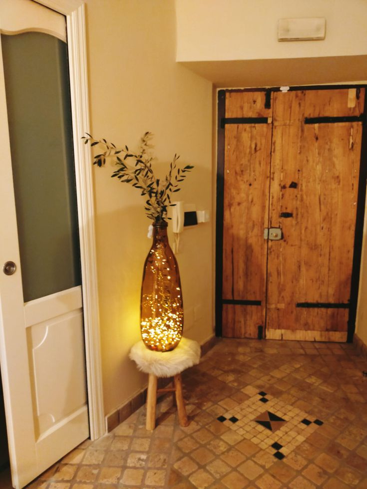 Un hall d'entrée simple avec une bouteille éclairée et une porte en bois. L'ambiance est décontractée et accueillante.