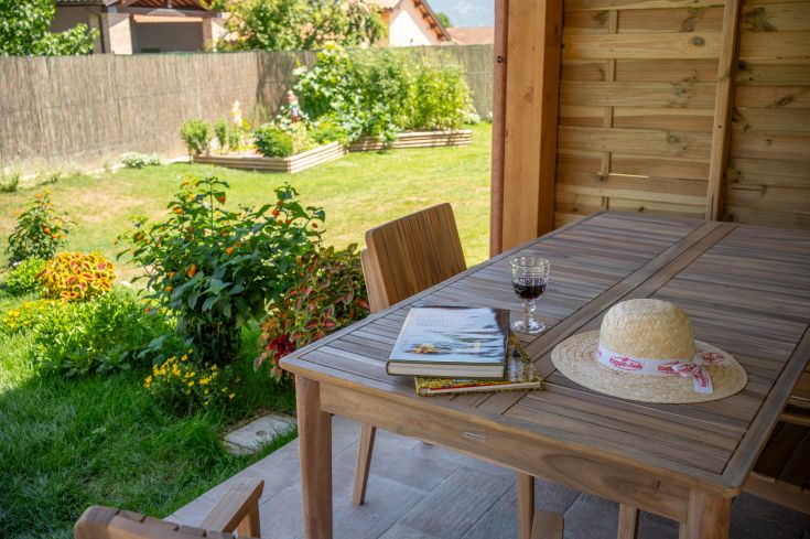 Un coin tranquille dans un jardin avec une table, un verre de vin et un chapeau entouré de fleurs.