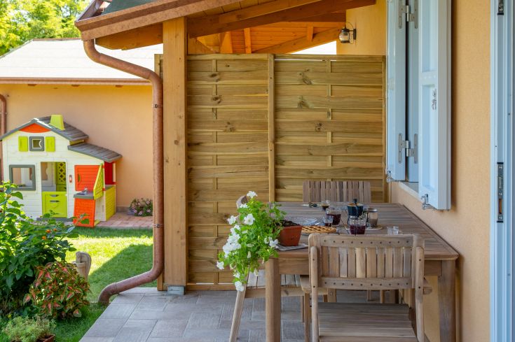 Un espace extérieur accueillant avec une table en bois entourée de plantes et de jouets pour enfants, idéal pour se détendre.
