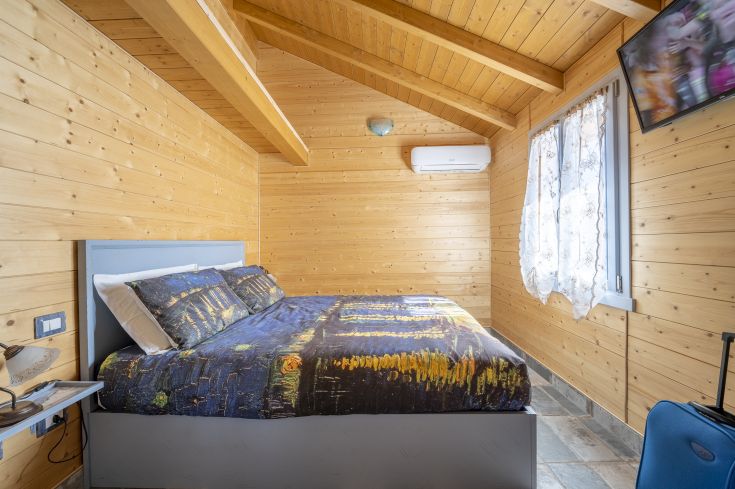 Une chambre en bois simple avec un lit aux couleurs vives et la climatisation.