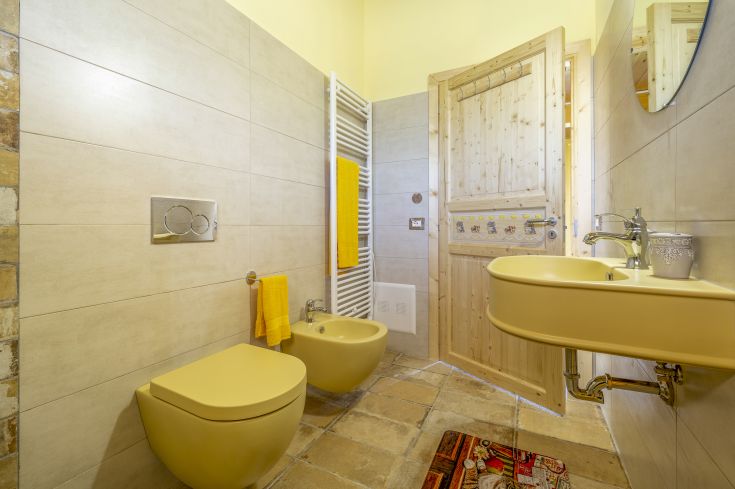 Salle de bain lumineuse avec des tons jaunes et des finitions en bois, espace idéal pour se détendre.